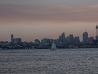 an ocean view of a skyline and skyscrapers at sunset in the background, including an airplane