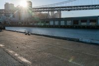 a couple of children and their skateboards near the water under a bridge that spans across a city street