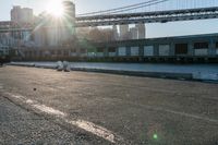 a couple of children and their skateboards near the water under a bridge that spans across a city street