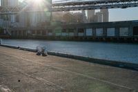 a couple of children and their skateboards near the water under a bridge that spans across a city street