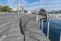 there is an empty wooden stage on a boardwalk near water and a city in the distance