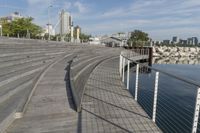 there is an empty wooden stage on a boardwalk near water and a city in the distance