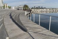 there is an empty wooden stage on a boardwalk near water and a city in the distance