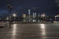 a view of new york city skyline at night from pier on the hudson river side