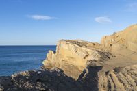 two people stand on the edge of a cliff next to the ocean in a bright blue sky