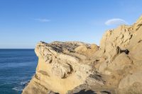 two people stand on the edge of a cliff next to the ocean in a bright blue sky