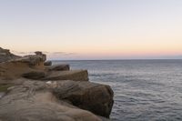 there is a rock ledge at the edge of the ocean at sunset on a clear day