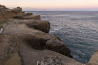 there is a rock ledge at the edge of the ocean at sunset on a clear day