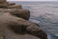 there is a rock ledge at the edge of the ocean at sunset on a clear day