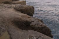 there is a rock ledge at the edge of the ocean at sunset on a clear day