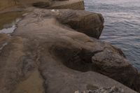 there is a rock ledge at the edge of the ocean at sunset on a clear day