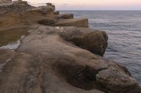 there is a rock ledge at the edge of the ocean at sunset on a clear day