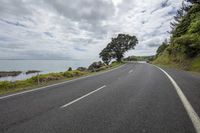 a single car drives along a country road beside the ocean on an overcast day