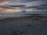 a lone surf board on the sand next to the ocean at dusk with clouds above