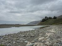 a rock shoreline with an overcast sky in the background and trees in the distance