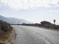 a empty road with a sign pointing right in front of it and mountains in the background