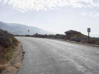 a empty road with a sign pointing right in front of it and mountains in the background