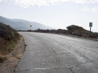 a empty road with a sign pointing right in front of it and mountains in the background