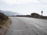 a empty road with a sign pointing right in front of it and mountains in the background