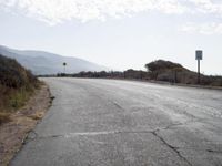 a empty road with a sign pointing right in front of it and mountains in the background