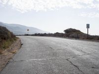 a empty road with a sign pointing right in front of it and mountains in the background