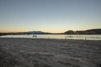 the empty area on the shore of a lake with mountains in the background at sunset