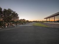 a bench sitting outside a building overlooking the water and sky at sunset at dusk with trees nearby