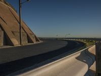 a traffic light next to an empty highway beside a hill under a blue sky and some light