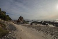 the light shines bright above the sand at the beach next to the water, with some rocks in the distance