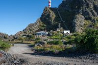 a dirt path and path up to a lighthouse next to a rock face covered mountain