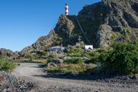 a dirt path and path up to a lighthouse next to a rock face covered mountain