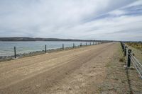 dirt road in front of water near a fenced off beach area with boats docked in the water