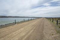 dirt road in front of water near a fenced off beach area with boats docked in the water