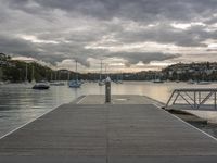 a dock with a number of boats in the water in front of buildings and a cloudy sky