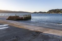 a wooden dock next to the ocean with waves hitting onto it at sunset, with hills in background