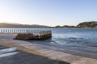 a wooden dock next to the ocean with waves hitting onto it at sunset, with hills in background