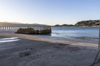 a wooden dock next to the ocean with waves hitting onto it at sunset, with hills in background