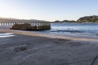 a wooden dock next to the ocean with waves hitting onto it at sunset, with hills in background