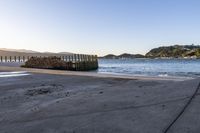 a wooden dock next to the ocean with waves hitting onto it at sunset, with hills in background