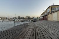 a dock with wooden boards and boats and buildings in the background at sunset near the ocean