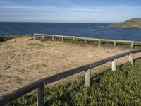 a fence near the ocean next to grass and beach rocks and water plants on the shore