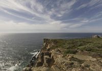 a man sitting on a cliff overlooking the ocean on a windy day with clouds in the sky