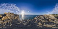 a panoramic view of the ocean with rocks and sand surrounding it and a cloudy sky