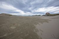 the large beach is surrounded by rocks and sand covered dunes in the distance is a calm body of water with many cliffs