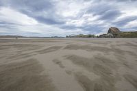 the large beach is surrounded by rocks and sand covered dunes in the distance is a calm body of water with many cliffs