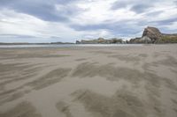 the large beach is surrounded by rocks and sand covered dunes in the distance is a calm body of water with many cliffs