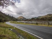 a bend in the road leads to the mountain side with low clouds overhead, and trees, along the sides