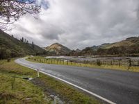 a bend in the road leads to the mountain side with low clouds overhead, and trees, along the sides