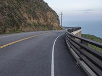 a curved road beside the ocean with rocky hills and a body of water in the background