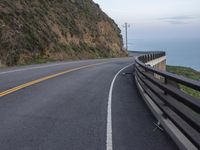 a curved road beside the ocean with rocky hills and a body of water in the background